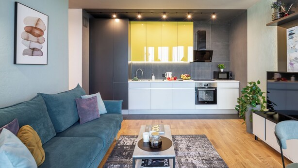 A modern living room with a sofa, coffee table, and a kitchen area in the background. - 2-Room Apart near the Botanical Garden (Minsk)