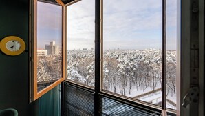 A room with a large window, a visible clock, and a view of a snowy landscape with buildings. - 2-Room Apart near the Botanical Garden (Minsk)