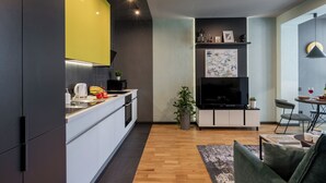 A modern kitchen with white cabinets, a yellow accent wall, and a dining area with a table and chairs. - 2-Room Apart near the Botanical Garden (Minsk)