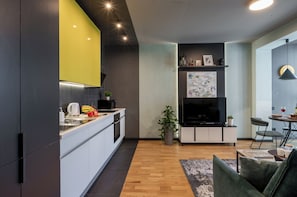 Een moderne keuken met witte kasten, een geel accentmuur en een eethoek met tafel en stoelen.
