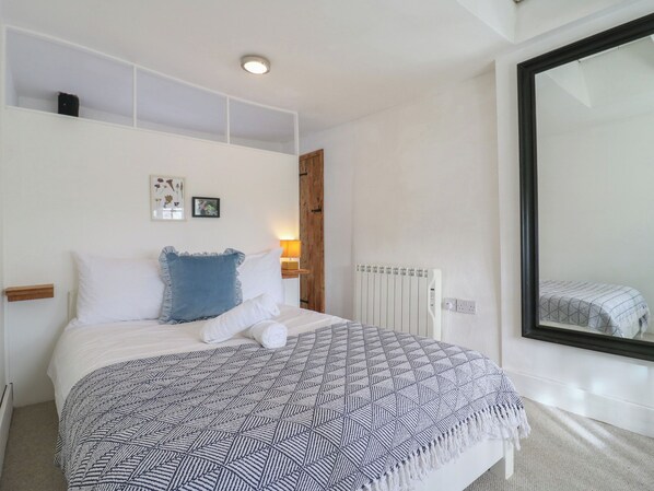Ein Schlafzimmer mit Bett, Nachttisch mit Lampe, Heizkörper und einem großen Spiegel.