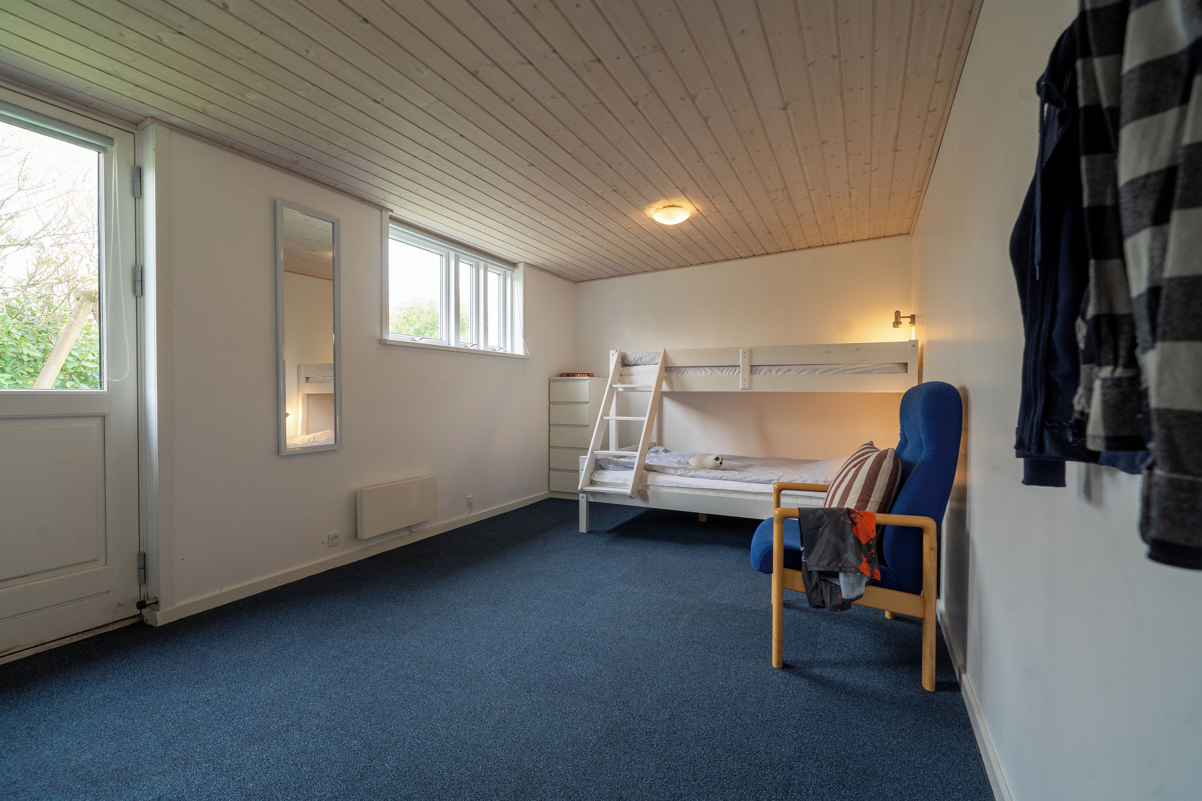 Ein Zimmer mit einem Etagenbett, einem Stuhl, einer Leiter, einem Fenster und einem Spiegel.