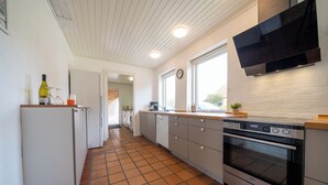 A modern kitchen with a built-in oven, a microwave, and a large window. - Feriehuset Fiskervej (Fjerritslev)