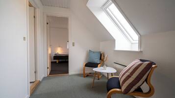 Une pièce chaleureuse avec un plafond en pente, une petite table ronde, deux chaises et un lit à l’arrière-plan.