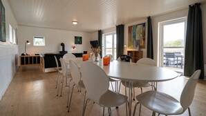 A dining area with a round table, white chairs, and a wooden bench. There is a small window and a painting on the wall. - Feriehuset Fiskervej (Fjerritslev)