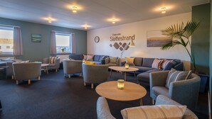 A hotel lobby with sofas, armchairs, a coffee table, a wall clock, a wall-mounted lamp, and a large window. - Feriehuset Fiskervej (Fjerritslev)
