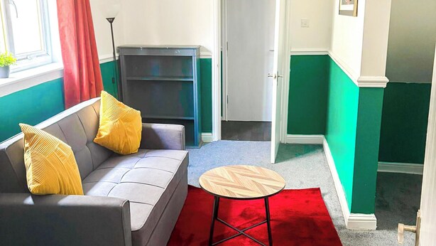 Un espacio habitable pequeño con un sofá gris, cortinas rojas, una mesita redonda y una alfombra roja.