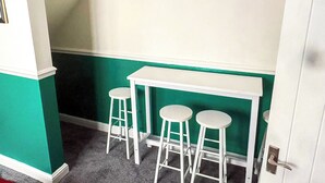 Una habitación pequeña con una mesa blanca y tres taburetes blancos. Las paredes están pintadas de verde y blanco.