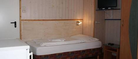 Una habitación pequeña y funcional con una cama individual, un televisor montado en la pared y un escritorio pequeño.
