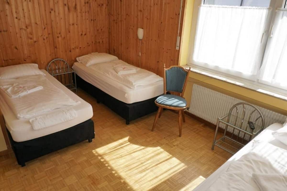 A room with two single beds, a chair, a radiator, and a window with curtains.
