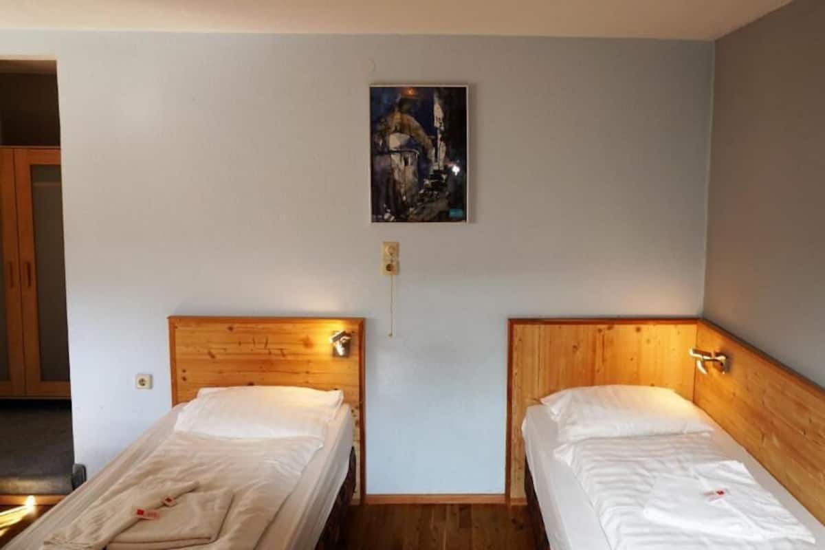 A room with two wooden beds, a nightstand, and a painting on the wall.