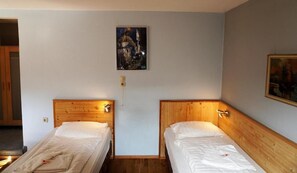 Une chambre avec deux lits en bois, une table de chevet et un tableau au mur.