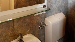A bathroom with a large mirror, a sink, and a toilet. There are three wall-mounted lights above the mirror. - Pension zur Rose (Schoenaich)