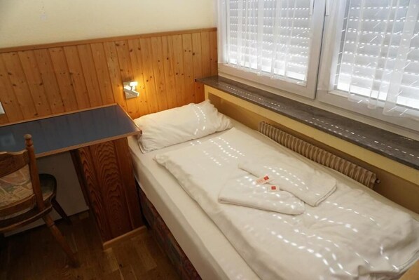 A small, cozy room with a wooden headboard, a single bed with white linens, a small table, and a chair. - Pension zur Rose (Schoenaich)