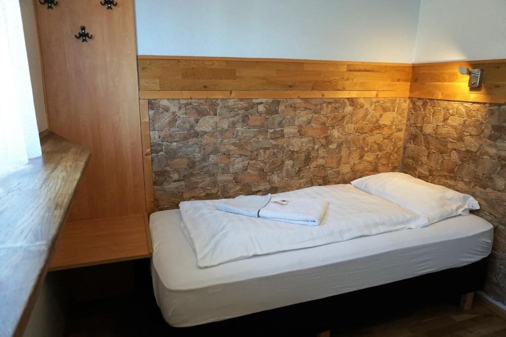 A bedroom with a stone wall, wooden headboard, and a bed with white linens.