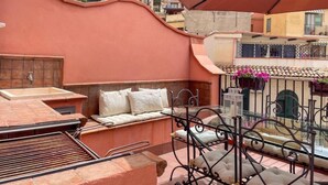 A rooftop terrace with a seating area, a grill, and a view of the cityscape.
