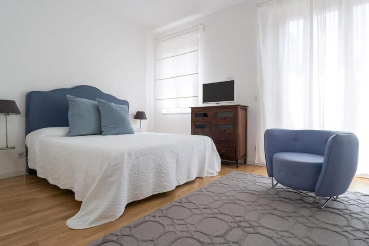 A bedroom with a bed, a dresser, a television, and a chair.