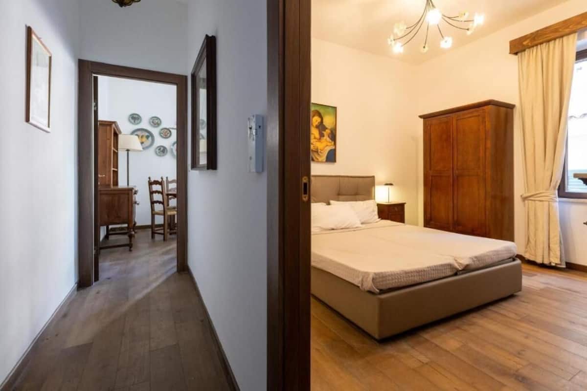 A bedroom with a bed, a wooden wardrobe, a nightstand, and a painting on the wall.