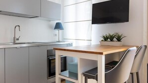 A modern kitchen with a built-in oven, a sink, and a flat-screen TV mounted on the wall.