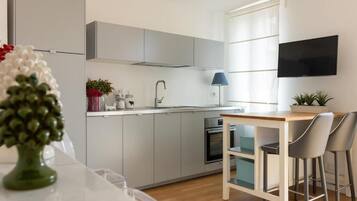 Una cocina moderna con armarios grises, horno empotrado, lavabo y comedor con una mesa y dos sillas.