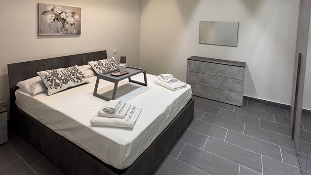 A modern bedroom with a large bed, bedside tables, a dresser, and a painting on the wall. - Oasis of relaxation in the heart of Altavilla Milicia, located between Palermo and Cefalù. (Altavilla Milicia)