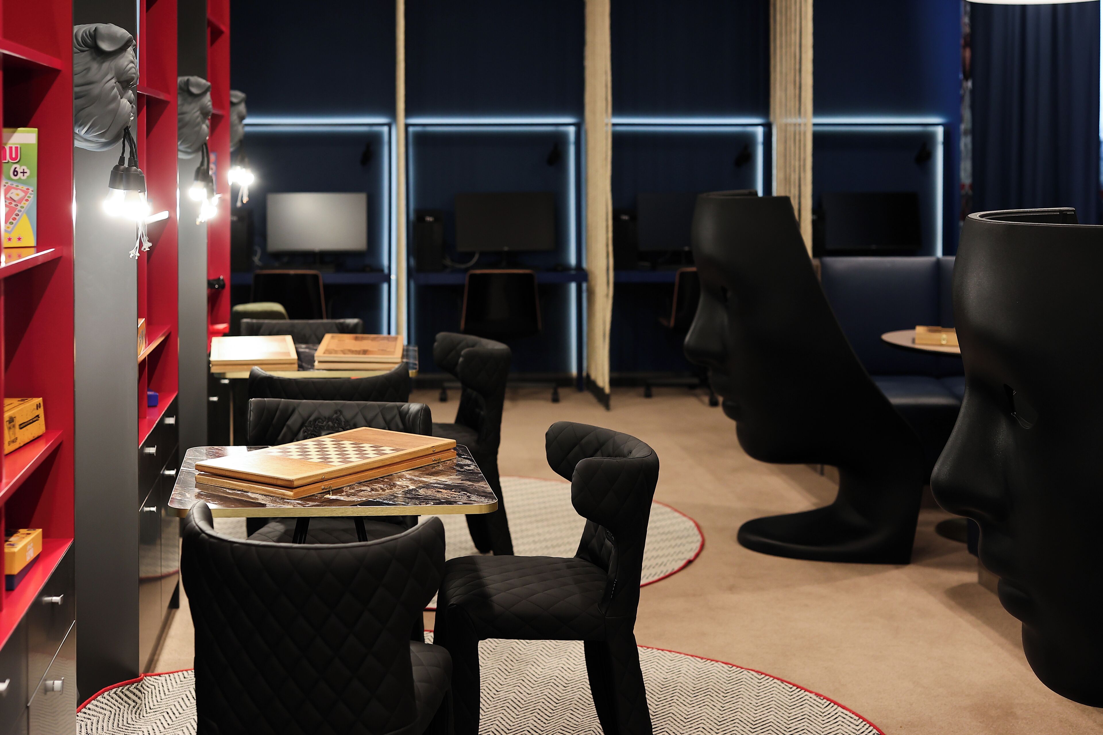 A modern room with a red bookshelf, black chairs, and a table with a book.