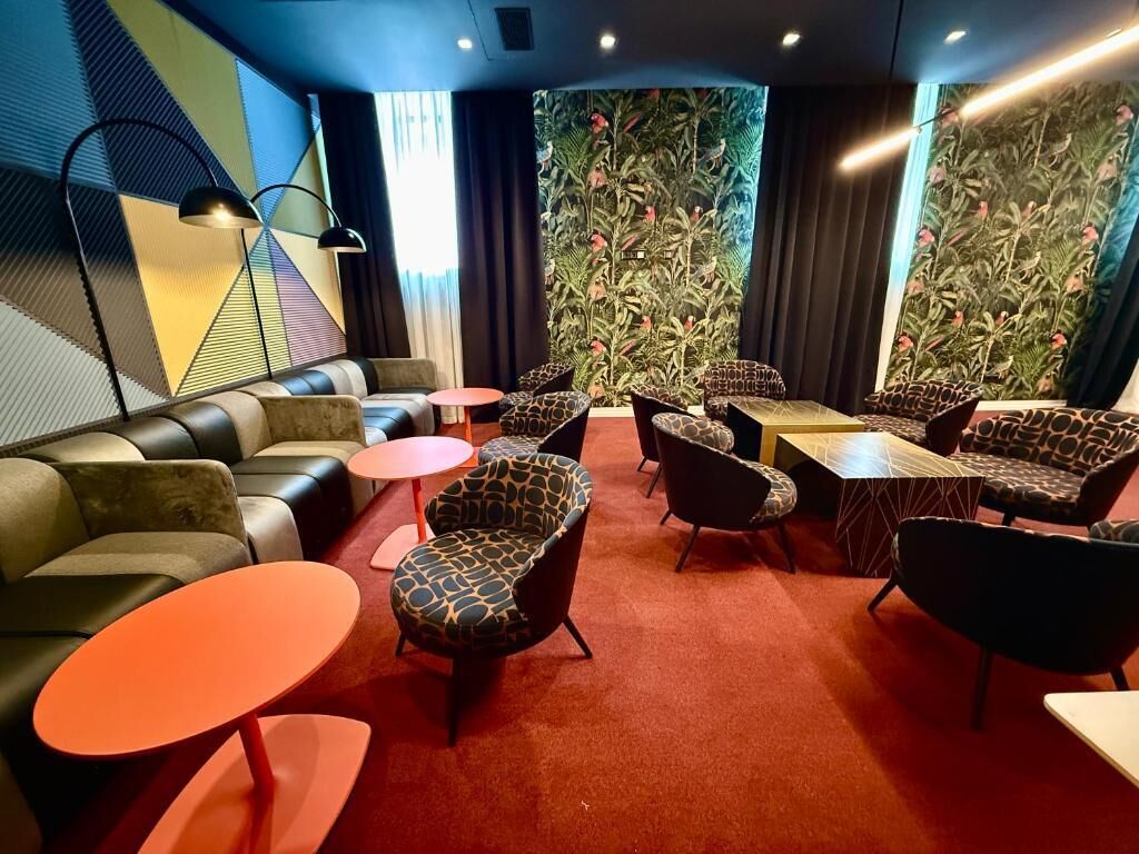 A modern lounge area with leather sofas, patterned armchairs, and small round tables.