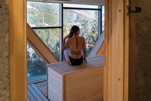 A person sitting on a wooden bench in a room with large windows, overlooking a mountainous landscape. - Moselle Armenia Wellness & Medical SPA (Jermuk)