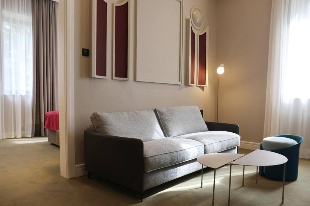 Una sala moderna con un sofá gris, una mesita blanca y un reposapiés azul.