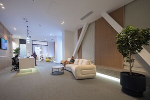 Un espacio de oficina moderno con un mostrador de recepción, un sofá blanco, una mesa de centro y una planta en maceta.