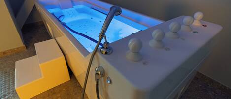 A modern spa tub with control knobs and a handheld showerhead.