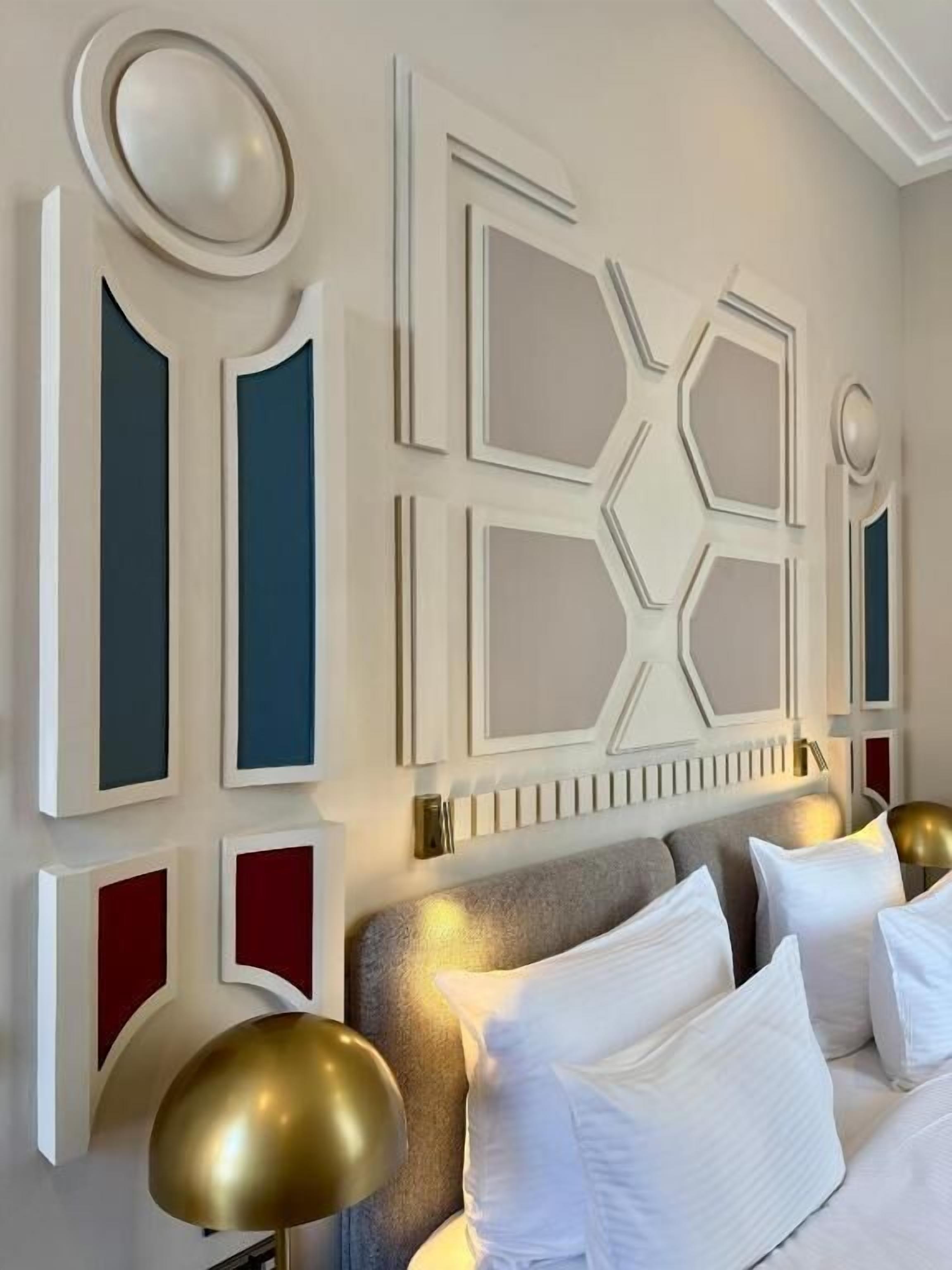 Ein modernes Schlafzimmer mit einem geometrischen Wandpaneel-Design, einem grauen Kopfteil und einer goldfarbenen Lampe.
