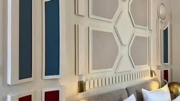 Ein modernes Schlafzimmer mit einem geometrischen Wandpaneel-Design, einem grauen Kopfteil und einer goldfarbenen Lampe.