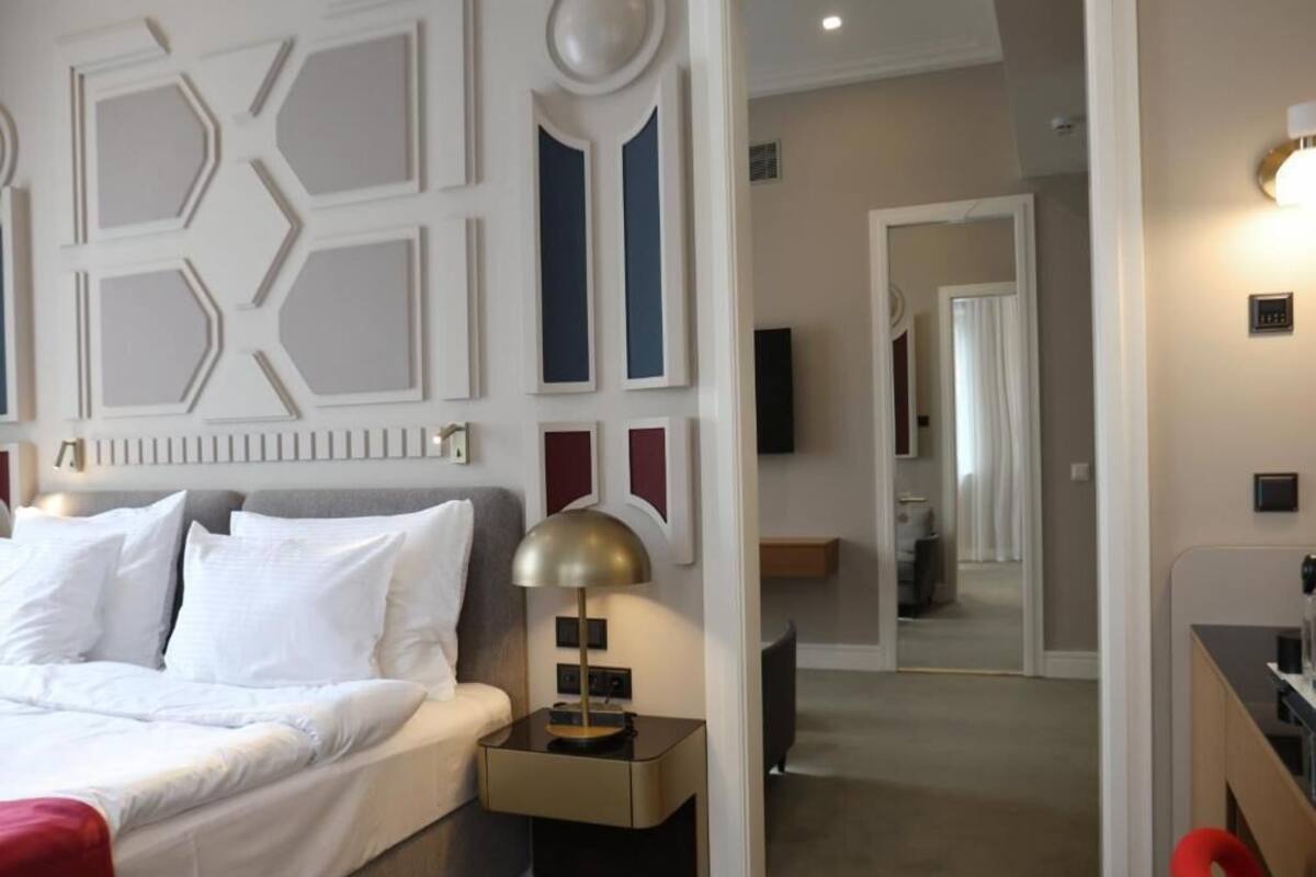 Una habitación de hotel con cama, mesita de noche, lámpara y espejo.