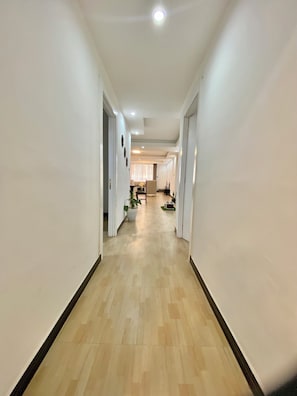 Un pasillo con suelo de madera, paredes blancas e iluminación empotrada en el techo.