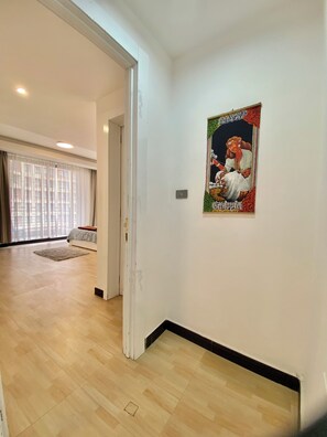 Una habitación con piso de madera, una cama, un ventanal con cortinas y un cartel en la pared.