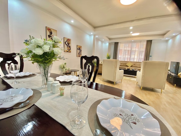 Un comedor con una mesa dispuesta para cuatro, sillas, un florero con flores y obras de arte en la pared.