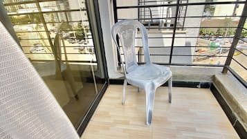 A balcony with a white plastic chair, a view of the cityscape, and a wooden floor.