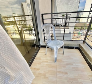 Un balcón con una silla de plástico blanca, vistas de la ciudad y suelo de madera.
