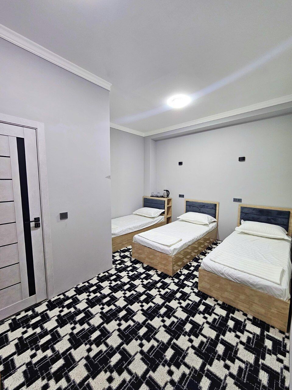 A room with three single beds, a patterned floor, and a white door.