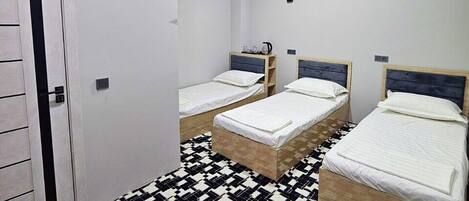 A room with three single beds, a patterned floor, and a white door.