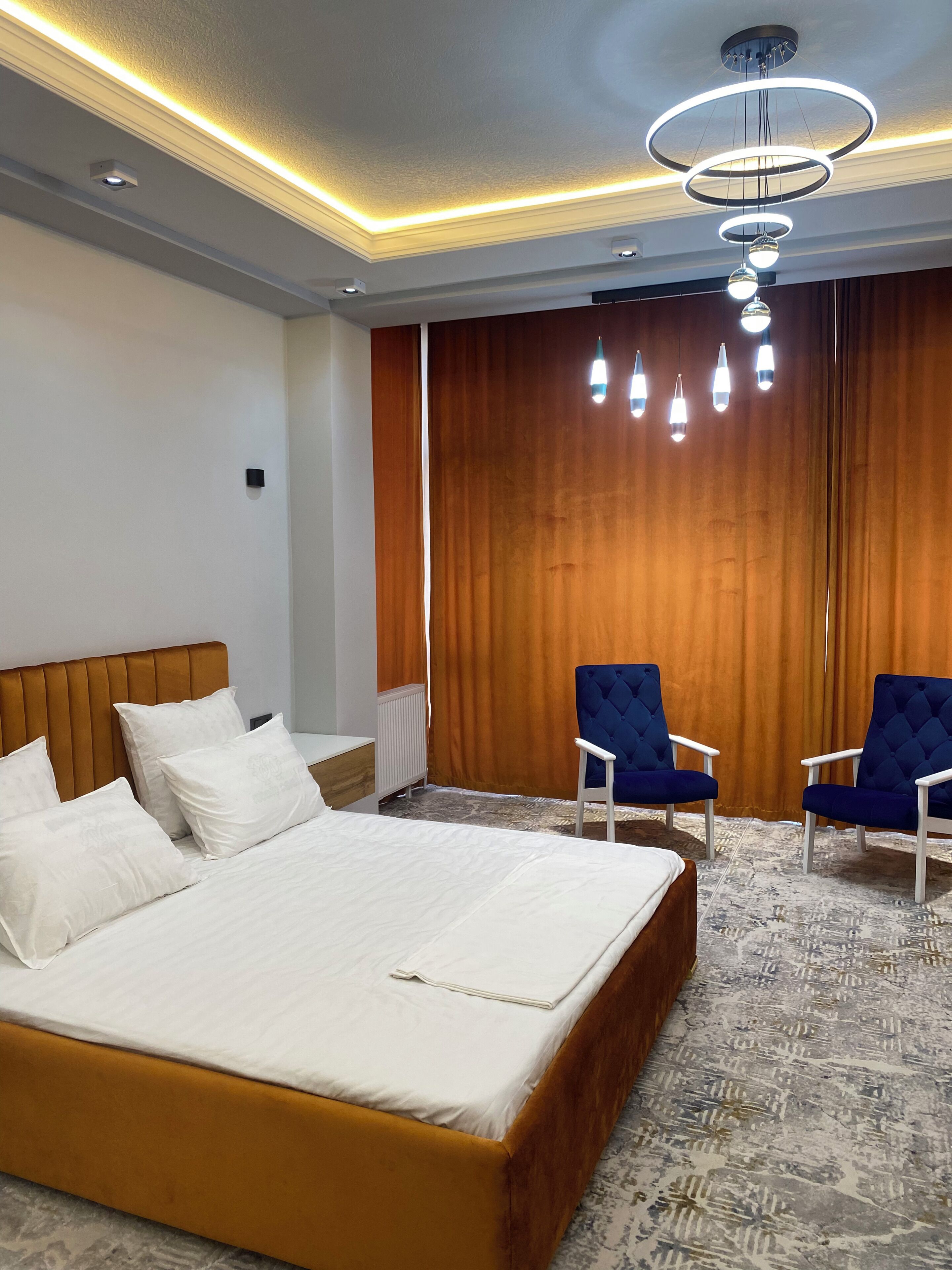 Una habitación de hotel con una cama grande, dos sillones, cabecera de madera y una lámpara de techo moderna.