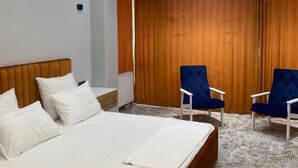 A hotel room with a large bed, two armchairs, a wooden headboard, a ceiling light fixture, and a patterned carpet. - Hectors Hotel (Kokand)