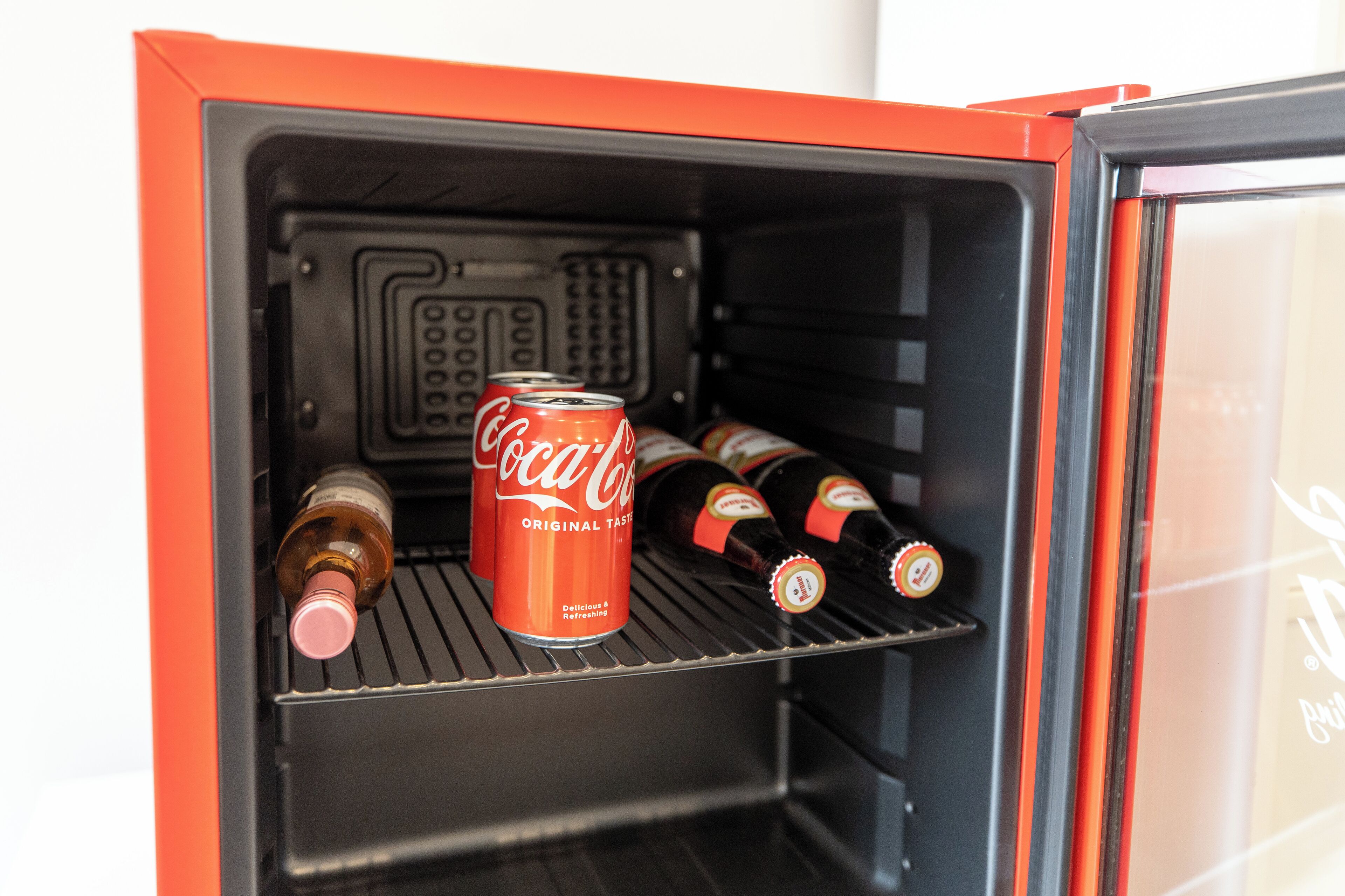Ein Kühlschrank mit einer Coca-Cola Dose und mehreren Flaschen.