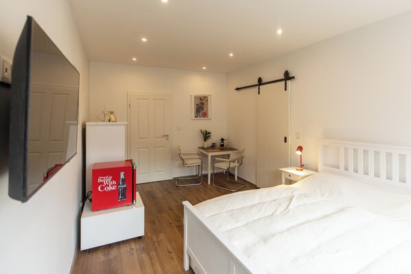A bedroom with a bed, a desk, a chair, a TV, and a red Coca-Cola box.
