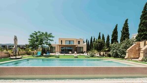 Un área de piscina moderna con sillones reclinables y un edificio al fondo.