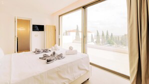 Una habitación de hotel con un ventanal grande, una cama con toallas, un televisor y una puerta.