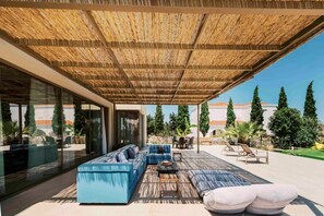 Un espace extérieur aménagé avec un coin salon abrité, comprenant un canapé bleu, une table à manger et une pergola au-dessus.