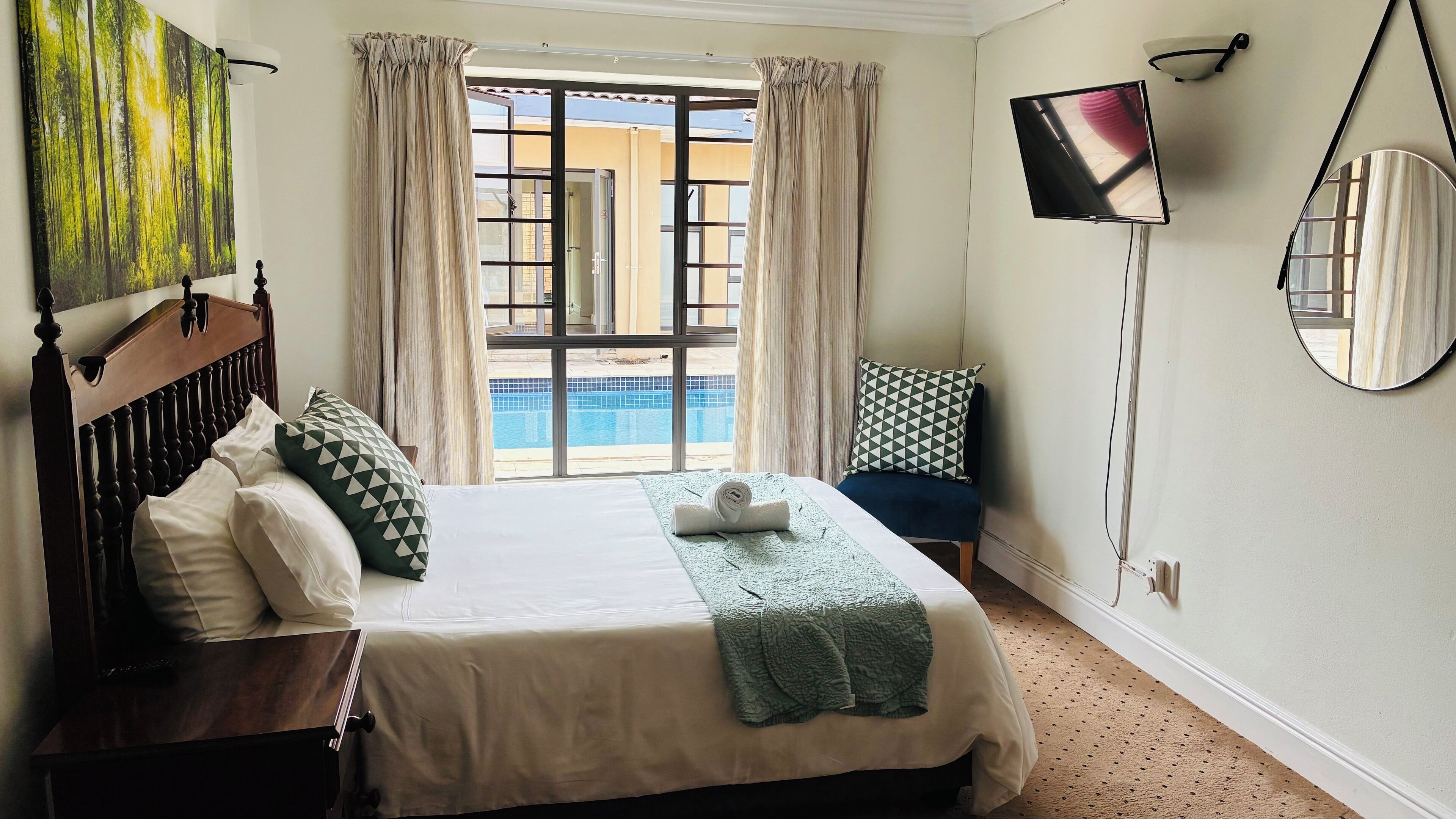 Une chambre d’hôtel avec un lit, une télévision, une grande fenêtre avec des rideaux, une vue sur la piscine et un miroir au mur.