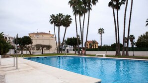 En swimmingpool med flisekant, omgivet af palmer og en bygning i baggrunden.